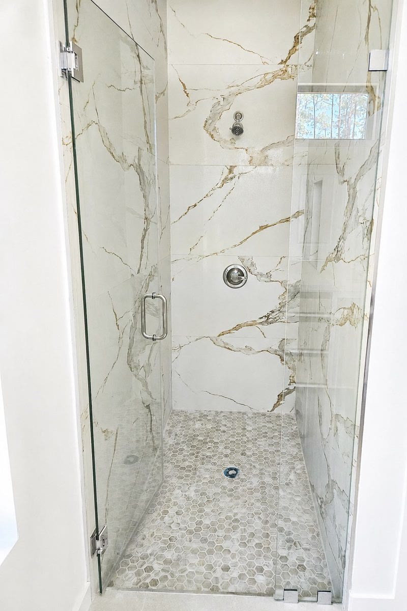 Primary bath shower with glass enclosure and marble-look wall